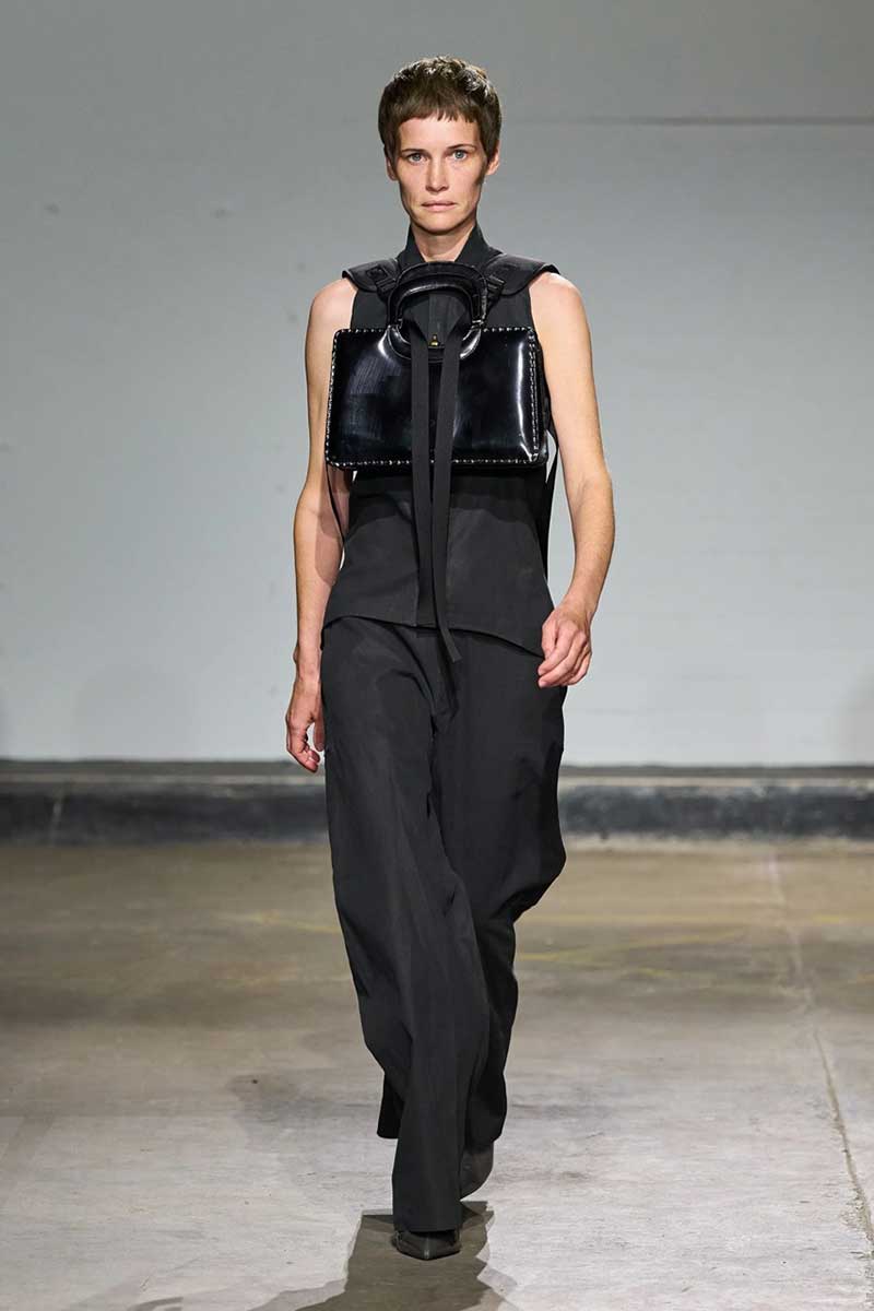 a man walking down a runway wearing a black outfit