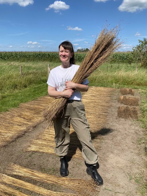 a woman holding a bundle of hay on a dirt road