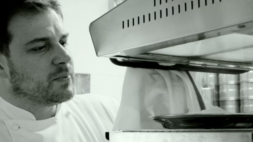 a man in a chef's outfit looking at something in the oven